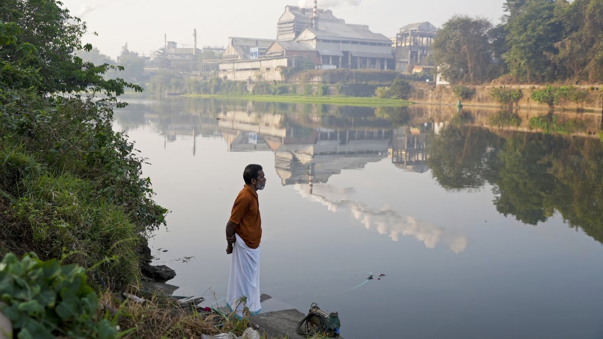 An Indian man stands on the bank of the Periyar River with smokestacks in the distance in Eloor, Kerala state, India, March 3, 2023. (AP Photo)