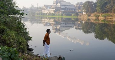 An Indian man stands on the bank of the Periyar River with smokestacks in the distance in Eloor, Kerala state, India, March 3, 2023. (AP Photo)