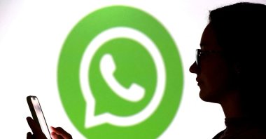A teenager poses for a photo while holding a smartphone in front of a WhatsApp logo in this illustration taken Sept.11, 2025. (Reuters File Photo)