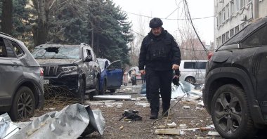 A Ukrainian law enforcement officer walks past damaged cars at the site of an air attack in Dnipro, Ukraine, Dec. 1, 2025. (AFP Photo) 