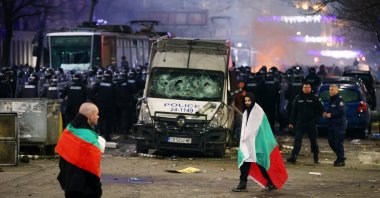 Police stand in formation as protesters walk covered by Bulgarian flags during a rally against austerity measures in next year&#039;s draft budget, in Sofia, Monday, Dec 1, 2025. (AP Photo)