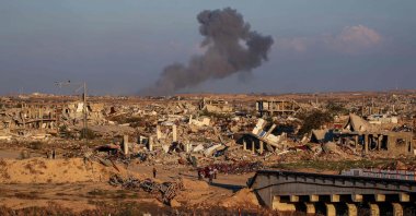 People walk amid the rubble of destroyed buildings at the Nuseirat camp for displaced Palestinians as smoke billows in the distance following Israeli strikes east of Gaza City, Dec. 2, 2025. (AFP Photo)