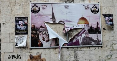 A cat sits next to a poster of slain Palestinian fighters that was torn during an Israeli raid, Old City of Nablus, occupied West Bank, Palestine, Dec. 6, 2025. (AFP Photo)