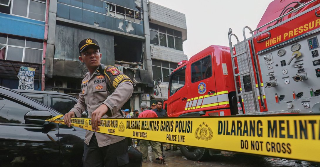 A member of the Indonesian police sets up a barricade tape to cordon off a seven-storey building where firefighters extinguished a fire that killed at least 20 people, Jakarta, Indonesia, Dec. 9, 2025. (AFP Photo)