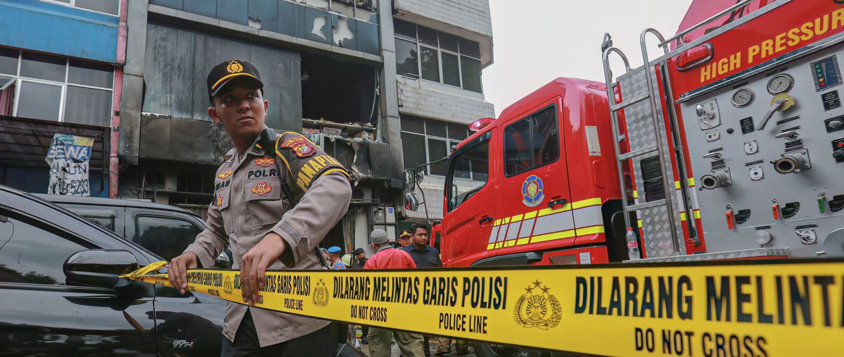 A member of the Indonesian police sets up a barricade tape to cordon off a seven-storey building where firefighters extinguished a fire that killed at least 20 people, Jakarta, Indonesia, Dec. 9, 2025. (AFP Photo)