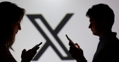Teenagers pose for a photo while holding smartphones in front of the X logo in this illustration, Sept. 11, 2025. (Reuters Photo)