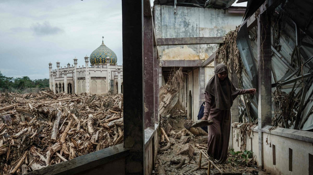 A middle school student who came with her teacher from Medang walks on a bench to avoid mud as piles of uprooted trees swept away by a flash flood remain at Darul Mukhlisin Islamic Boarding School and its attached mosque, Aceh Tamiang, Northern Sumatra, Indonesia, Dec. 14, 2025. (AFP photo)