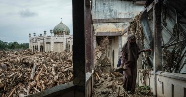 A middle school student who came with her teacher from Medang walks on a bench to avoid mud as piles of uprooted trees swept away by a flash flood remain at Darul Mukhlisin Islamic Boarding School and its attached mosque, Aceh Tamiang, Northern Sumatra, Indonesia, Dec. 14, 2025. (AFP photo)