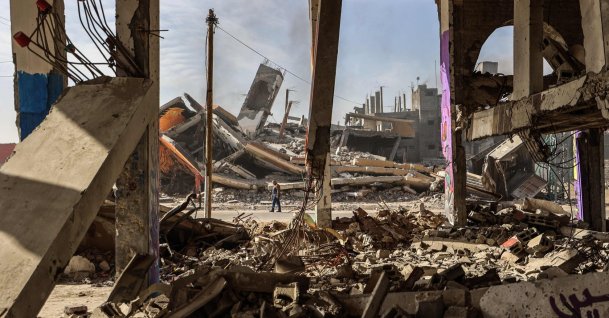 A man carrying walks past destroyed buildings partially covered in murals in the Maghazi refugee camp outside Deir al-Balah, Dec. 8, 2025. (AFP Photo)