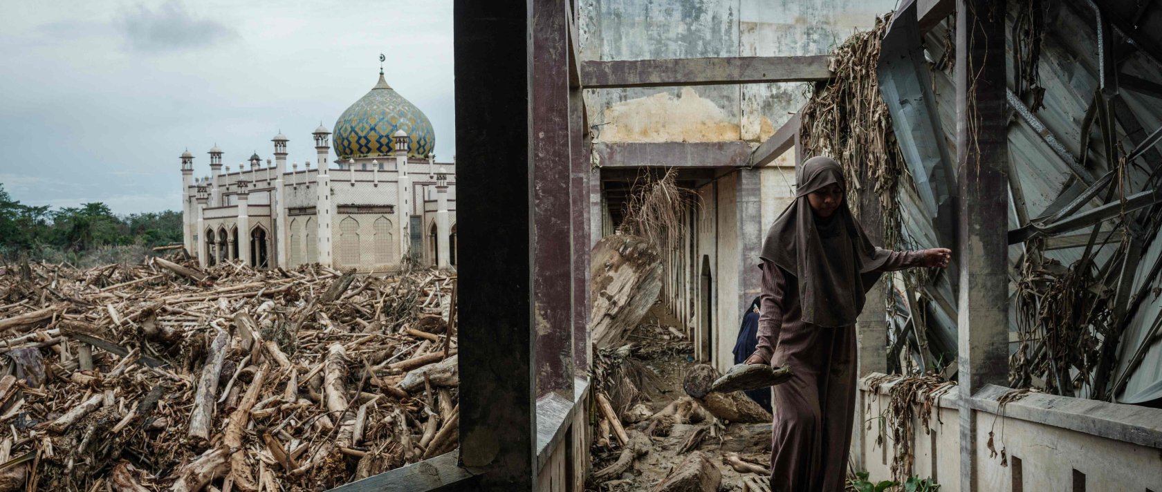 A middle school student who came with her teacher from Medang walks on a bench to avoid mud as piles of uprooted trees swept away by a flash flood remain at Darul Mukhlisin Islamic Boarding School and its attached mosque, Aceh Tamiang, Northern Sumatra, Indonesia, Dec. 14, 2025. (AFP photo)