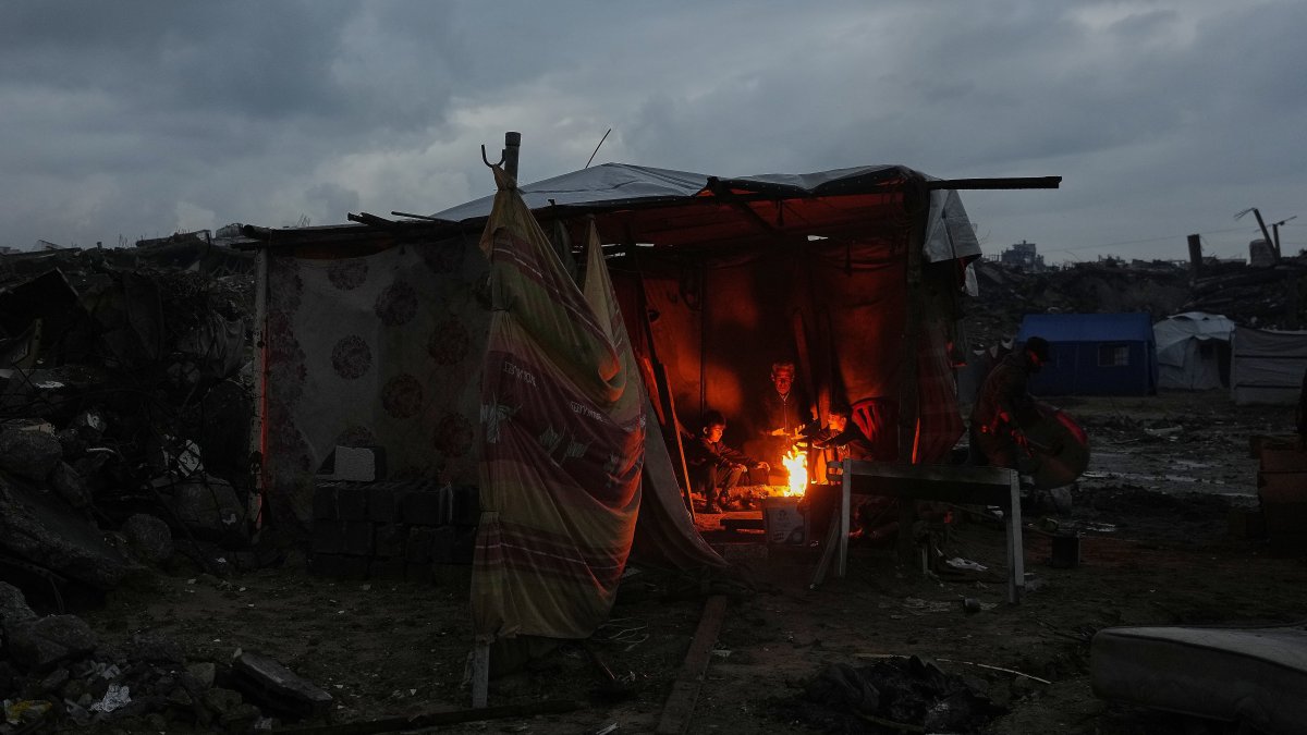 Aziz Halawa, 60, sits with his children as they warm themselves next to the fire inside their tent amid the destruction left by the Israeli air and ground operations, Gaza City, Palestine, Dec. 12, 2025. (AP Photo)