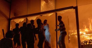 People are seen at the entrance to the Daily Star building as it burns amid protests following the news of the death of youth leader Sharif Osman Hadi, Dhaka, Bangladesh, Dec. 19, 2025. (AFP Photo)