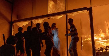 People are seen at the entrance to the Daily Star building as it burns amid protests following the news of the death of youth leader Sharif Osman Hadi, Dhaka, Bangladesh, Dec. 19, 2025. (AFP Photo)