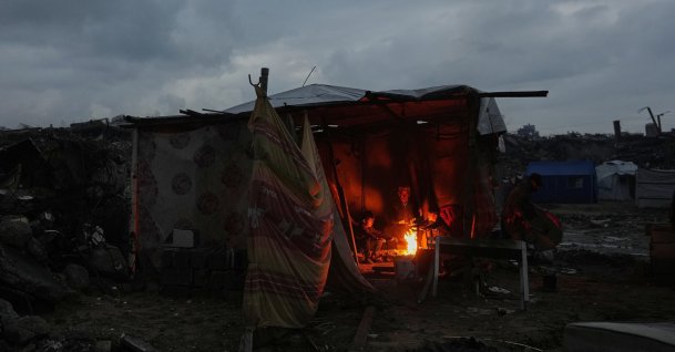 Aziz Halawa, 60, sits with his children as they warm themselves next to the fire inside their tent amid the destruction left by the Israeli air and ground operations, Gaza City, Palestine, Dec. 12, 2025. (AP Photo)