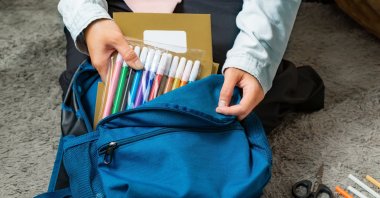 A mother prepares and packs her child’s school supplies into a school bag. (Shutterstock Photo)