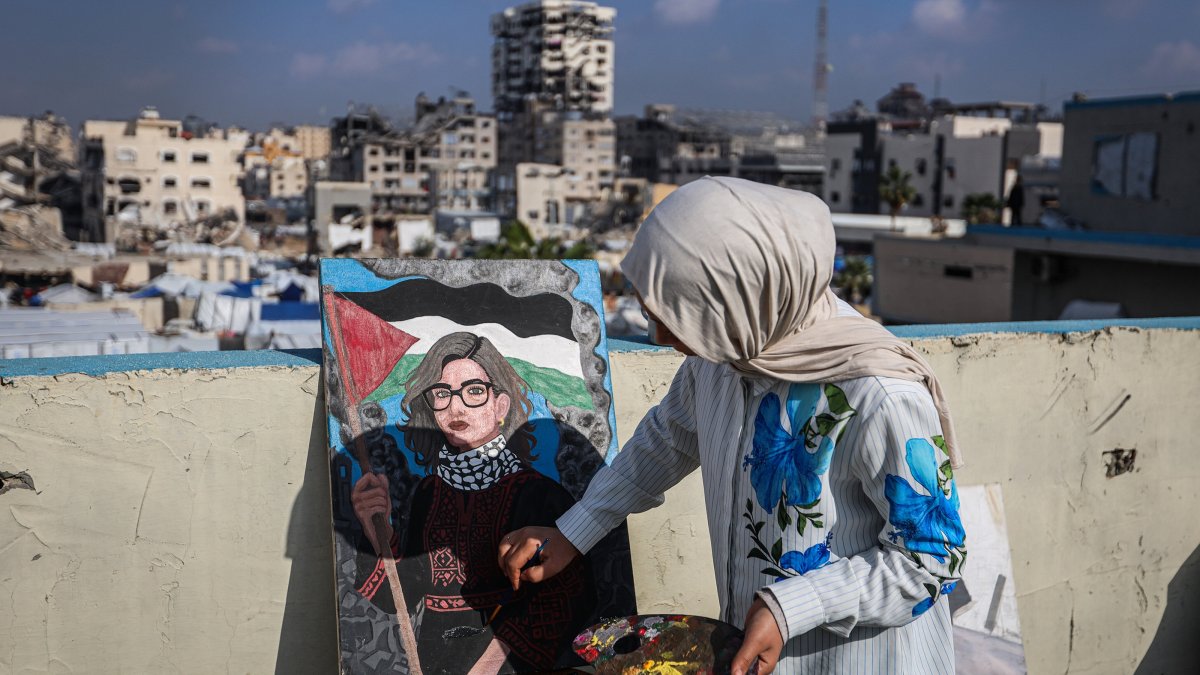 Fifteen-year-old painter Sara Abu Saade paints with the destroyed buildings of Gaza City in the background, Gaza Strip, Palestine, Dec. 23, 2025. (AA Photo)