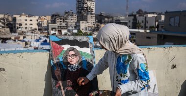 Fifteen-year-old painter Sara Abu Saade paints with the destroyed buildings of Gaza City in the background, Gaza Strip, Palestine, Dec. 23, 2025. (AA Photo)