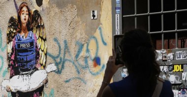 A woman takes a picture of the image "The Angel", painted earlier this year by street artist Harry Greb, dedicated to journalists killed in Gaza, showing an angel wearing a bulletproof vest with the word "Press" written on it and holding the body of a child, Rome, Italy, Aug. 25, 2025. (AP Photo)