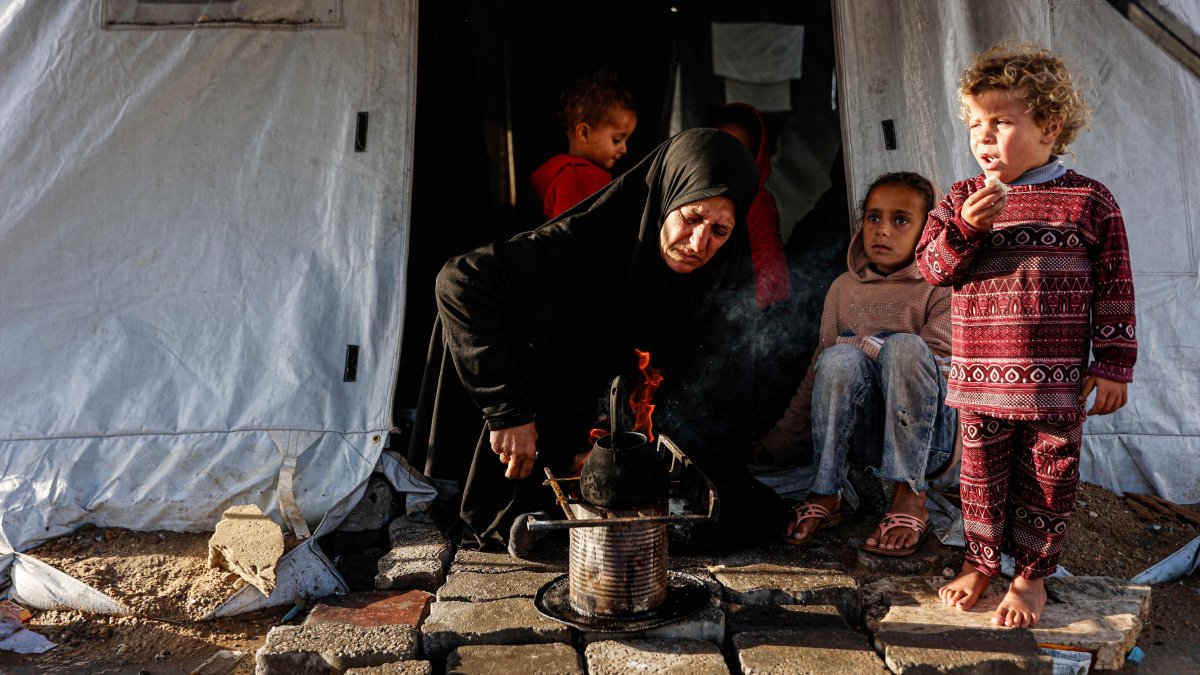 A displaced Palestinian woman heats a pot as children look on outside her tent-home as the region experiences rain and cold winter conditions, in Gaza City, Palestine, Dec. 28, 2025. (AFP Photo)
