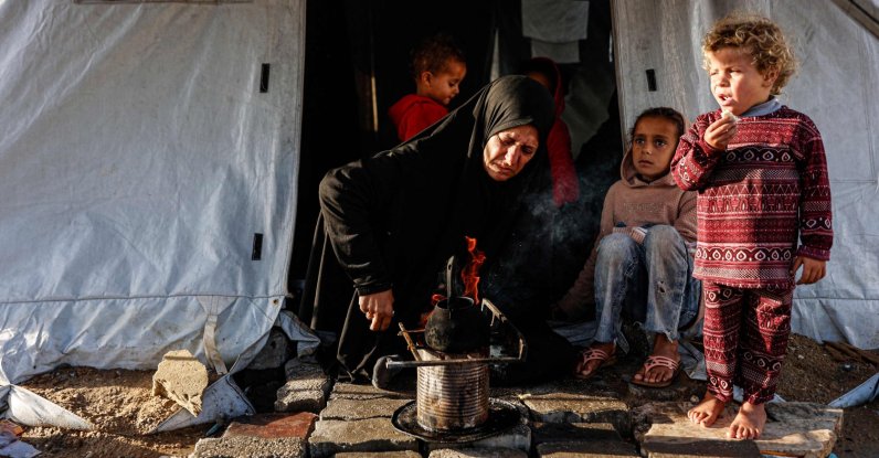 A displaced Palestinian woman heats a pot as children look on outside her tent-home as the region experiences rain and cold winter conditions, in Gaza City, Palestine, Dec. 28, 2025. (AFP Photo)
