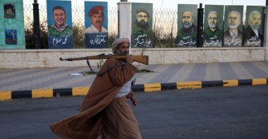 An armed man walks past paintings on display on a fence in Sana'a, Yemen, Dec. 28, 2025. (EPA Photo)