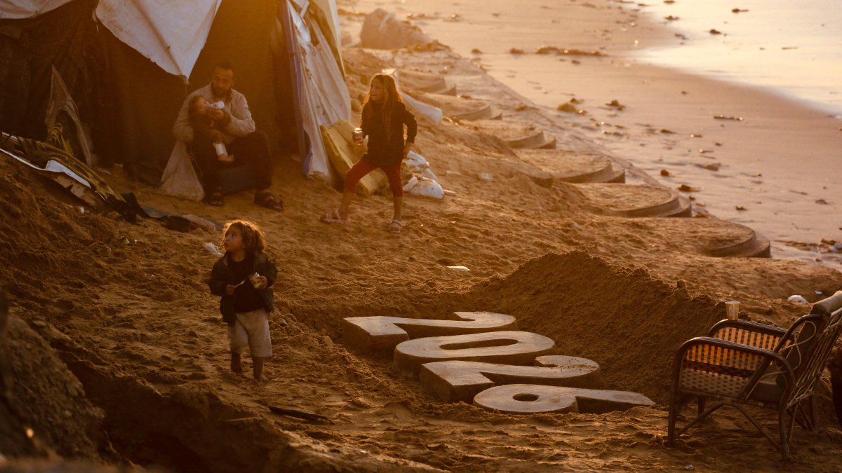 A man feeds a child as children walk next to a sand sculpture by Artist Yazed Abo Jarad of the coming year, as displaced Palestinians prepare to usher in the New Year in Deir al-Balah in the central Gaza Strip, Palestine, Dec. 30, 2025. (AFP Photo)