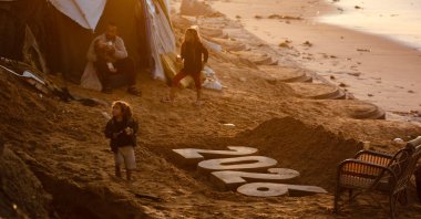 A man feeds a child as children walk next to a sand sculpture by Artist Yazed Abo Jarad of the coming year, as displaced Palestinians prepare to usher in the New Year in Deir al-Balah in the central Gaza Strip, Palestine, Dec. 30, 2025. (AFP Photo)
