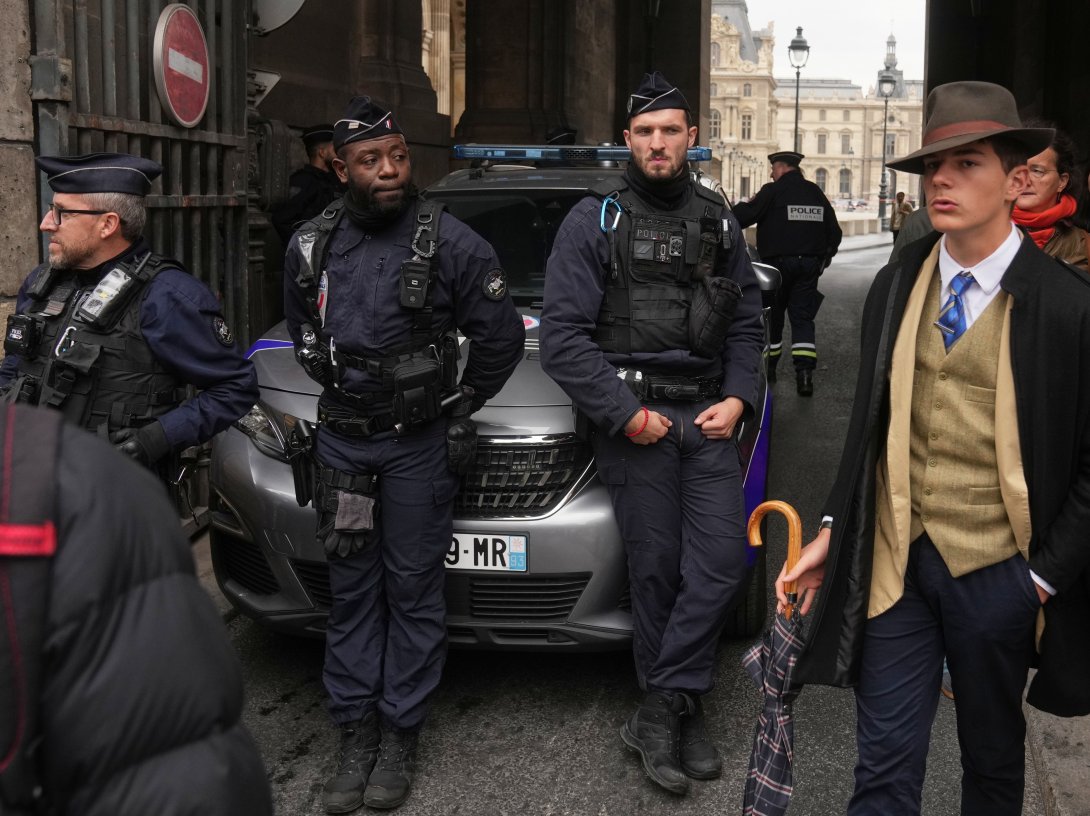 Pedro Elias Garzon Delvaux (R) walks past as police officers block an entrance to the Louvre after thieves carried out a daylight raid on French crown jewels, Paris, France, Oct. 19, 2025. (AP Photo)