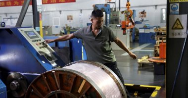 An employee works next to a reel of copper flat wire on the production line at the Wellascent factory in Ganzhou, Jiangxi province, China, Aug. 14, 2025. (Reuters Photo)