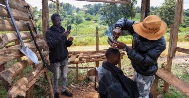 Barber and content creator Safari Martins uses a clothing iron as he shaves Ian Njenga in Kiambu, Kenya, Nov. 26, 2025. (AP Photo)