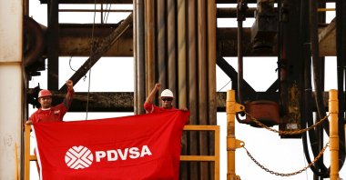 Oilfield workers hold a flag with the corporate logo of Venezuela's state oil company PDVSA, in a drilling rig at an oil well operated by them, in the oil rich Orinoco belt, near Cabrutica at the state of Anzoategui, Venezuela, April 16, 2015. (Reuters Photo)