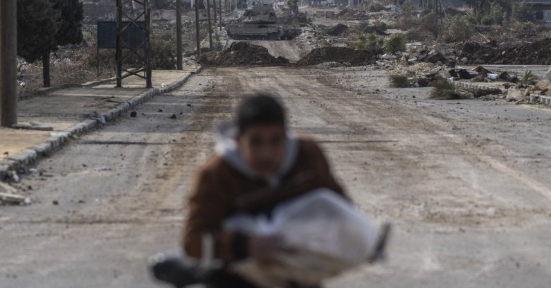 This file photo shows a boy carrying bread cycling home as Israeli military armored vehicles block a road leading to the town of Quneitra, Syria, Jan. 5, 2025. (AP Photo)