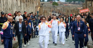 Actor Jackie Chan holds the Olympic torch as it passes through the Archaeological Park, Pompeii, Italy, Dec. 22, 2025. (AP Photo)