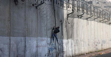 A Palestinian man climbs using a rope over a section of an illegal Israeli barrier that separates the West Bank from Jerusalem, Jan. 3, 2026. (AFP Photo)