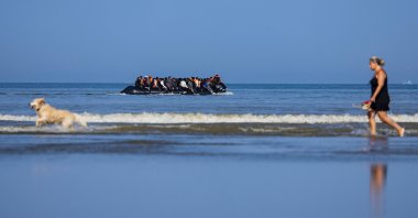 A tourist walks her dog as migrants board a smuggler's boat in an attempt to cross the English Channel off the beach of Hardelot in Neufchatel-Hardelot, northern France, June 30, 2025. (AFP Photo)