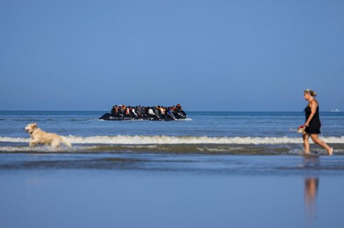 A tourist walks her dog as migrants board a smuggler's boat in an attempt to cross the English Channel off the beach of Hardelot in Neufchatel-Hardelot, northern France, June 30, 2025. (AFP Photo)
