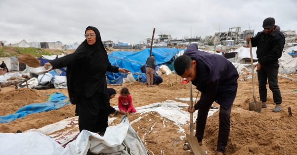 A Palestinian man shovels the sand off the tarpauling of a tent, the day after the Israeli military shelled a tented camp housing displaced families, in the Al-Shati refugee camp, in Gaza City, Jan. 9, 2026. (AFP Photo)