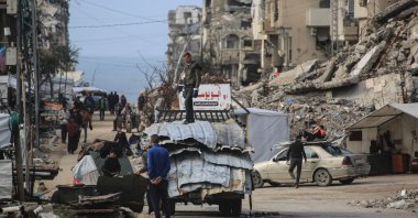 A man stands on a truck loaded with metal sheets as people make their way amid damaged buildings in Jabalia, in the northern Gaza Strip, Jan. 10, 2026. (AFP Photo)