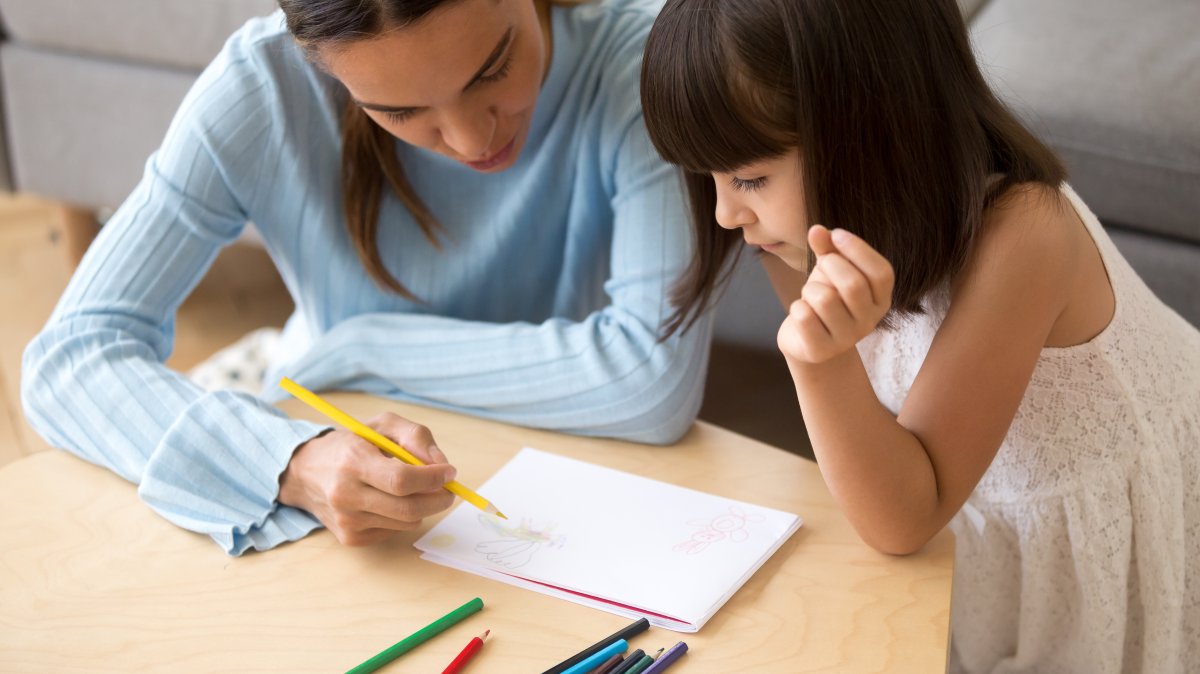 A mother helps her daughter draw with colored pencils during a home-based learning activity. (Shutterstock Photo)
