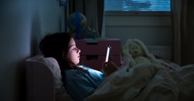 A child uses a smartphone lying in bed late at night. (Shutterstock Photo)