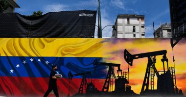A man wearing a face mask walks past a mural depicting an oil pump and the Venezuelan flag in a street of Caracas, Venezuela, May 26, 2022. (AFP Photo)