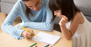 A mother helps her daughter draw with colored pencils during a home-based learning activity. (Shutterstock Photo)