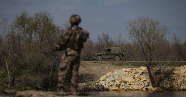 A Greek army vehicle, background, drives past in front of a Turkish special forces team (L), patrolling along the Meriç (Maritsa) River, Turkish-Greek border, Edirne, Türkiye, March 11, 2020. (AP Photo)