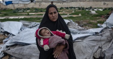 A Palestinian woman carries her infant as her family is trying to gather what remains of their belongings after their tent was damaged in Khan Younis in the southern Gaza Strip, Jan. 9, 2026. (EPA Photo)