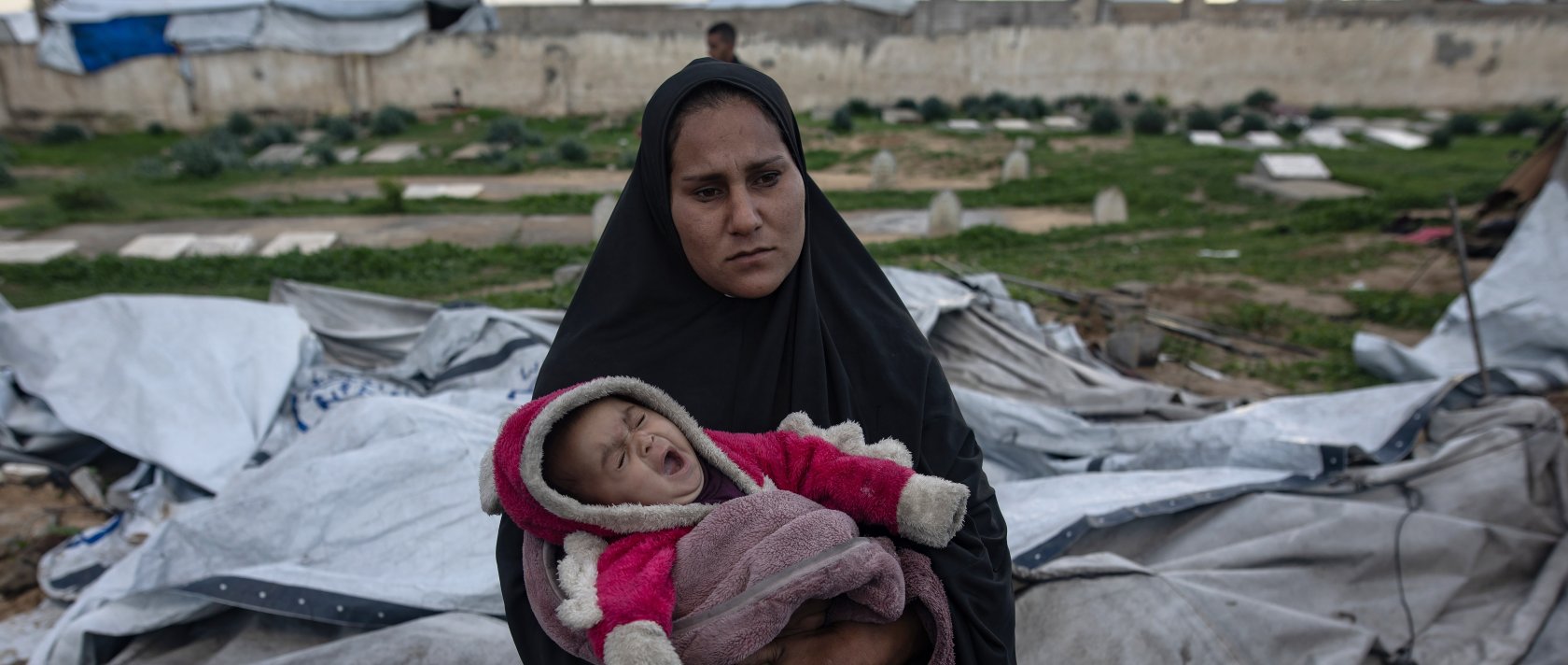 A Palestinian woman carries her infant as her family is trying to gather what remains of their belongings after their tent was damaged in Khan Younis in the southern Gaza Strip, Jan. 9, 2026. (EPA Photo)