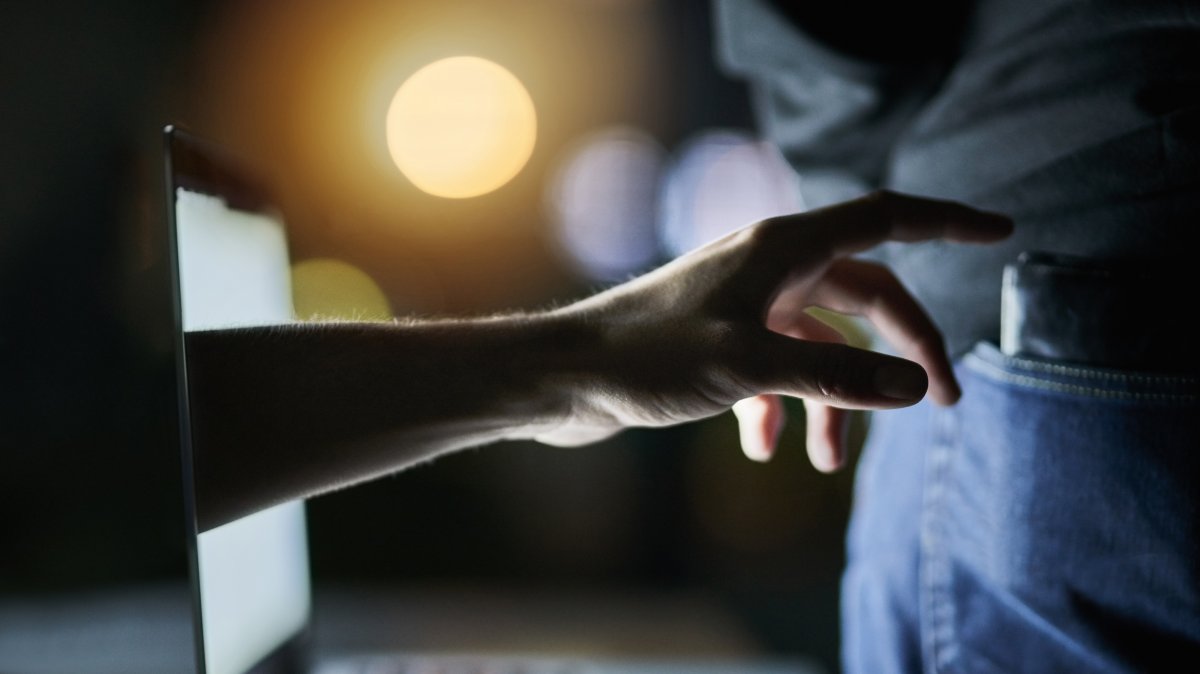A laptop, a hand and a wallet as the hand attempts to pickpocket a victim. (Shutterstock Photo)