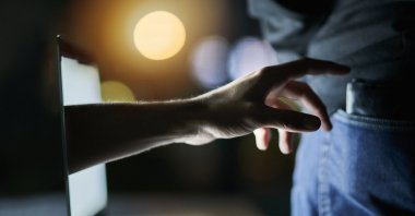 A laptop, a hand and a wallet as the hand attempts to pickpocket a victim. (Shutterstock Photo)