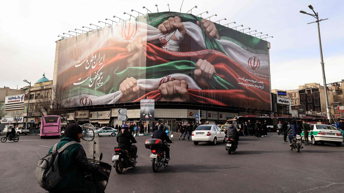 Vehicles pass by a large patriotic banner depicting the Iranian flag on Enghelab Square, Tehran, Iran, Jan. 14, 2026. (AFP Photo)