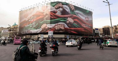 Vehicles pass by a large patriotic banner depicting the Iranian flag on Enghelab Square, Tehran, Iran, Jan. 14, 2026. (AFP Photo)