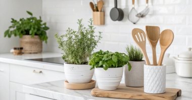 Potted herbs and wooden utensils sit on a white marble countertop in a bright, inviting kitchen. (Shutterstock Photo)